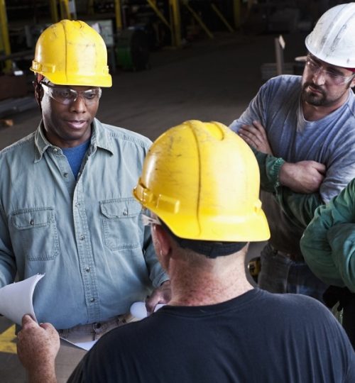 Diverse team of workers in fabrication shop, looking at plans.